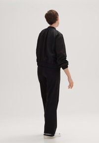 Czarna kurtka typu bomber z elastycznymi mankietami i dołem, zestawiona z czarnymi spodniami i białymi sneakersami. Gładka tkanina o minimalistycznym designie.