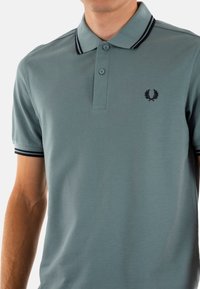 Polo shirt azzurro chiaro realizzato in tessuto testurizzato, caratterizzato da un collo a strisce scure a contrasto, una patta con due bottoni e un logo ricamato sul petto.