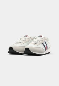 Sneaker bianche e beige con suole nere, lacci bianchi e strisce rosse, bianche e blu con il marchio "Tommy Jeans" sui lati.