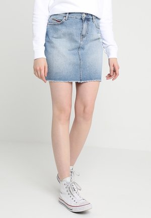 Jupe en denim mini en bleu clair, finition délavée avec un ourlet effiloché. Présente des poches avant et une taille standard, associée à des baskets montantes blanches.
