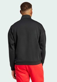 Svart sweatshirt med hög krage, nedliftade axlar och ribbade ärmslut. Slät textur med avslappnad passform, kombinerad med röda byxor.