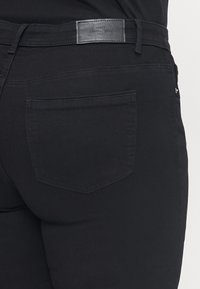 Black denim jeans featuring a mid-rise waist, back pocket with a triangular design, and a leather brand patch at the waistband.