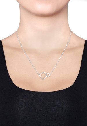 Silberne geometrische Halskette mit zwei sich überlappenden Quadraten an einer zarten Kette, vor einem schlichten Hintergrund.