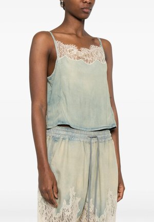 Donna che indossa un top azzurro chiaro senza maniche con rifinitura in pizzo e pantaloni larghi abbinati con dettagli in pizzo sui lati e vita con coulisse.