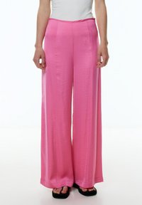 Weite Hosen in leuchtendem Pink, aus einem glatten, leichten Stoff gefertigt. Mit hoher Taille und subtiler Textur.