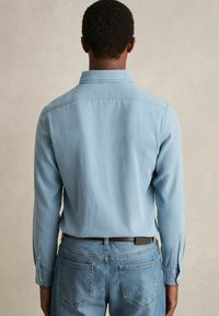 Lichtblaues overhemd met lange mouwen, gemaakt van zachte stof, heeft knoopmanchetten en een getailleerde pasvorm, gecombineerd met blauwe denim jeans.