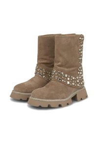 Bottes en suédine marron à semelle plate. Elles présentent des clous en argent décoratifs et un bord métallique contrastant autour de la cheville. Design épais et texturé.