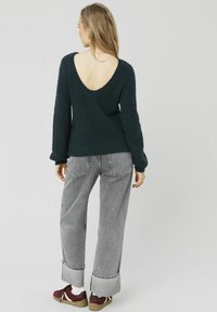 Pull en tricot vert avec un dos en V profond, des manches longues et un tissu texturé. Associé à un jean gris à jambes larges et des baskets bordeaux.