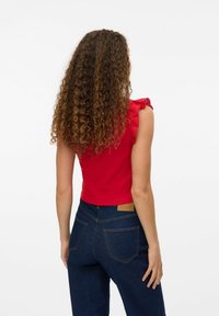 Rode cropped top met kanten ruche schouderbanden; gecombineerd met donkere denim high-waisted jeans met achterzakken en een leren merklabel.