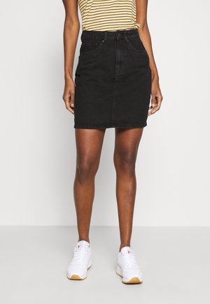 Falda de denim negra con un diseño ajustado, cintura alta y bolsillos delanteros, combinada con una camiseta de rayas y zapatillas blancas.