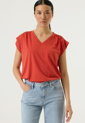 Rood T-shirt met V-hals en korte mouwen, zachte textuur en een ontspannen pasvorm, gecombineerd met lichtblauwe spijkerbroek met voorzakken.