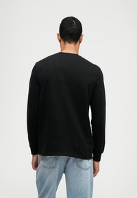 Camisola preta de mangas longas com decote redondo, feita de um tecido suave. Apresenta um design simples, e a pessoa está a usar jeans azul claro.