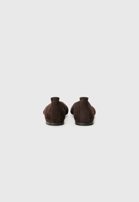 Des chaussures slip-on en suede marron présentant un bout arrondi, des panneaux latéraux élastiques et une semelle plate noire. Le matériau a une texture douce.