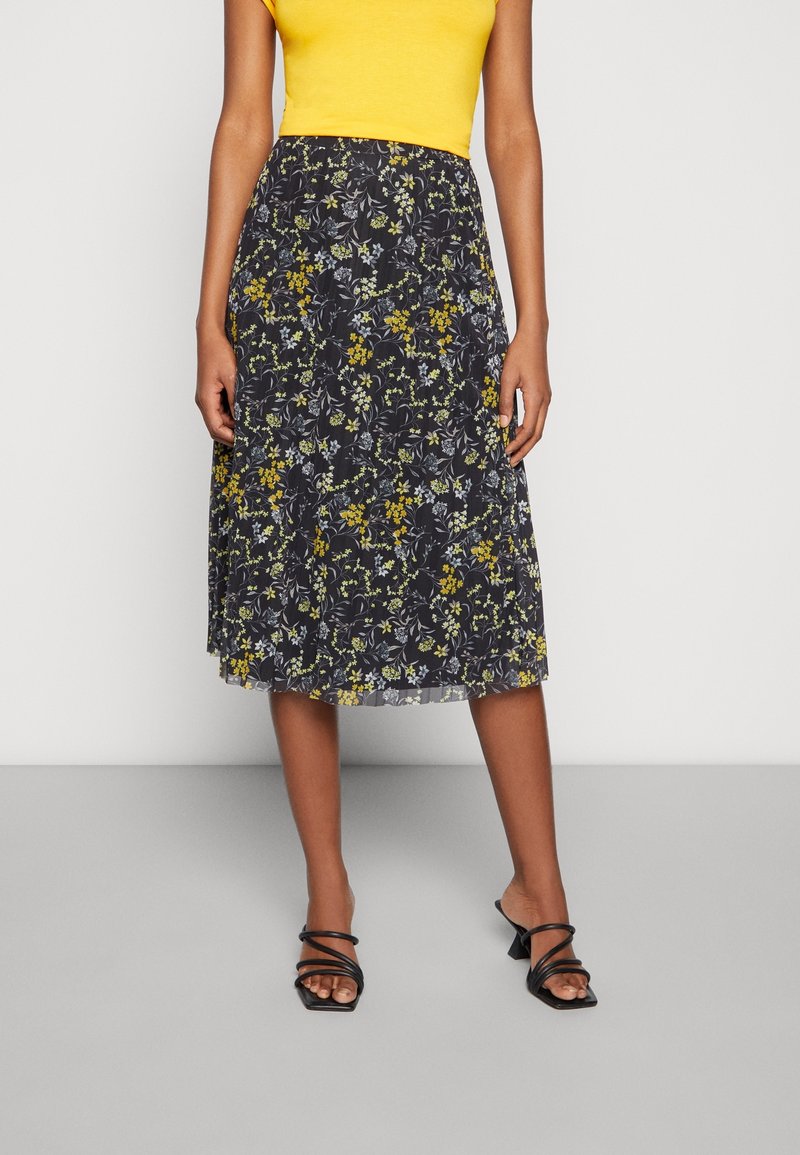 Black floral skirt with yellow and green patterns, pleated texture, knee-length cut, paired with a yellow top and black strappy sandals.