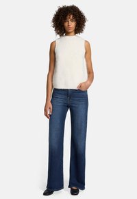 Top senza maniche bianco e soffice con scollo tondo, abbinato a jeans a palazzo blu scuro e scarpe nere chiuse, con dettagli minimi.