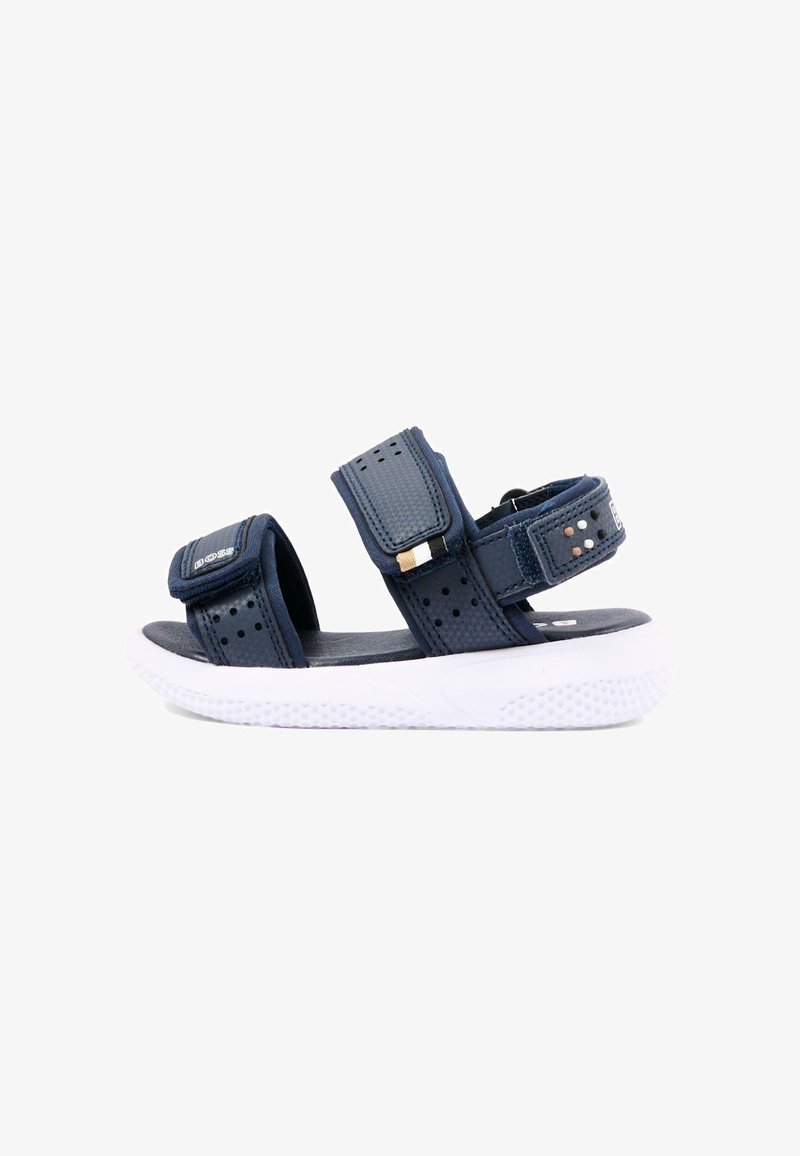 Sandale bleu marine avec sangles Velcro réglables et semelle blanche rembourrée, conception à orteils et talon ouverts pour un usage décontracté.