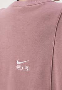 Růžová mikina s žebrovaným výstřihem, se stříbrně vyšitým logem Nike a textem "AIR". Měkký materiál, minimalistický design, bez vzorů.