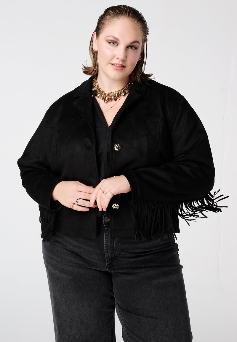Zwarte suède cropped jas met franjes, zilverkleurige knopen en een losse pasvorm. Gecombineerd met donkere jeans voor een monochrome uitstraling.