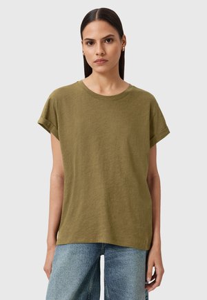 Olijfgroene katoenen T-shirt met een ronde halslijn en omgeslagen korte mouwen. Ontwerp met een relaxte pasvorm, gedragen met lichtblauwe wijde jeans.