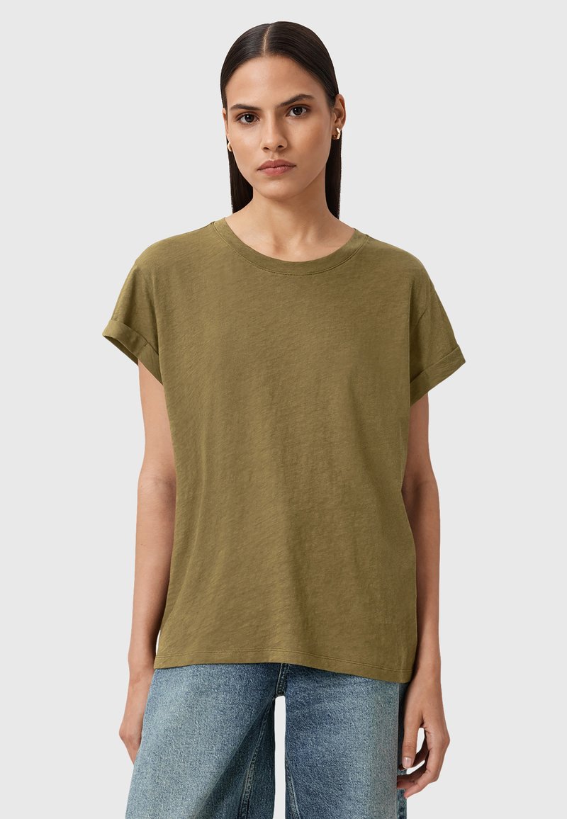 Olivenfarbene Baumwoll-T-Shirt mit Rundhalsausschnitt und umgeschlagenen kurzen Ärmeln. Lässiger Schnitt, kombiniert mit hellblauen weiten Jeans.