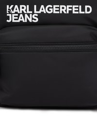 Μαύρο σακίδιο από νάιλον με φερμουάρ και λευκό λογότυπο "KARL LAGERFELD JEANS". Απαλή υφή με μινιμαλιστικό σχέδιο.