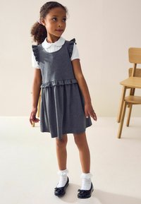 Grå bomulls klänning med volangdetaljer, kombinerad med en vit skjorta med krage. Svarta lackskor och vita fräna strumpor fulländar outfiten.