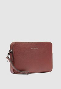 Pochette in pelle marrone con una consistenza liscia, chiusura con zip e cinturino da polso staccabile. Presenta un design minimalista e un logo in rilievo.