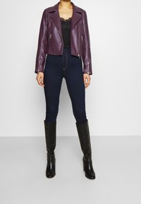 Veste courte en cuir bordeaux avec des fermetures éclair argentées, débardeur en dentelle noir, jean skinny bleu foncé et bottes noires à talons hauts arrivant au genou.