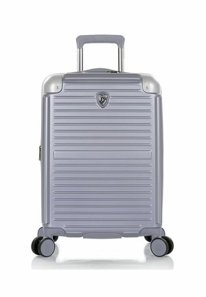 Valise rigide argentée avec des rainures horizontales, quatre roues doubles pivotantes, une poignée extensible et un petit badge logo au centre avant.