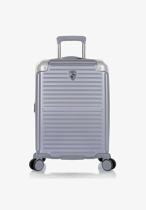 Valise rigide argentée avec des rainures horizontales, quatre roues doubles pivotantes, une poignée extensible et un petit badge logo au centre avant.