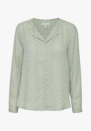 Lichtgroene blouse gemaakt van zachte stof, met een v-hals, lange mouwen en witte stippen op een gladde textuur.