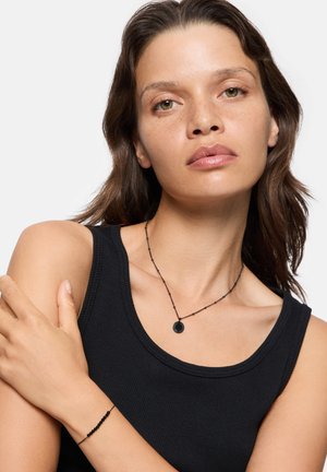 Black beaded necklace with a circular pendant, featuring a delicate chain and complementary black bracelet, modeled with a fitted black tank top.