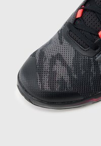 Μαύρο αθλητικό παπούτσι με επάνω μέρος από δίχτυ, με υφασμένο σχέδιο και έντονες κόκκινες λεπτομέρειες. Εν ισχυμένη μύτη και ελαστική σόλα εμφανείς.