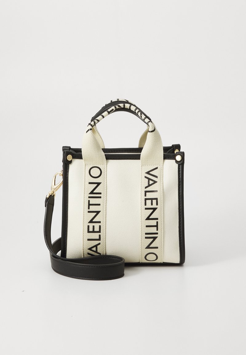Λευκή καμβά τσάντα με μαύρες λεπτομέρειες και λαβές. Διαθέτει δύο μαύρες λωρίδες με το κείμενο "VALENTINO". Περιλαμβάνει αποσπώμενη μαύρη ζώνη ώμου.