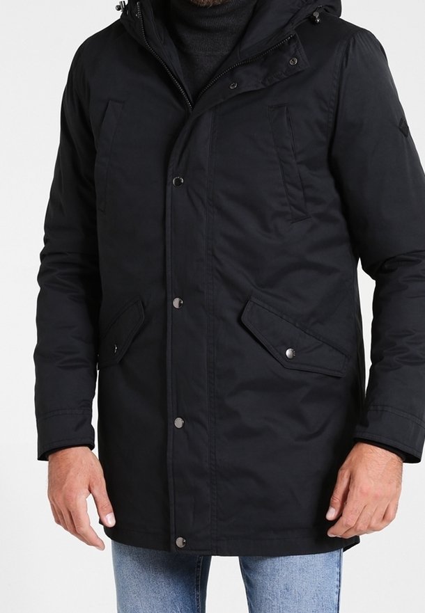 Homme portant un manteau d'hiver noir à capuche avec boutons-pression et poches à rabat, assorti à un jean bleu clair.