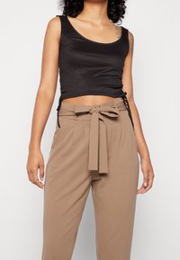 Czarny prążkowany crop top z szerokimi ramiączkami i wiązaniami po bokach, połączony z beżowymi spodniami o wysokim stanie z ozdobnym wiązaniem w pasie i plisami.