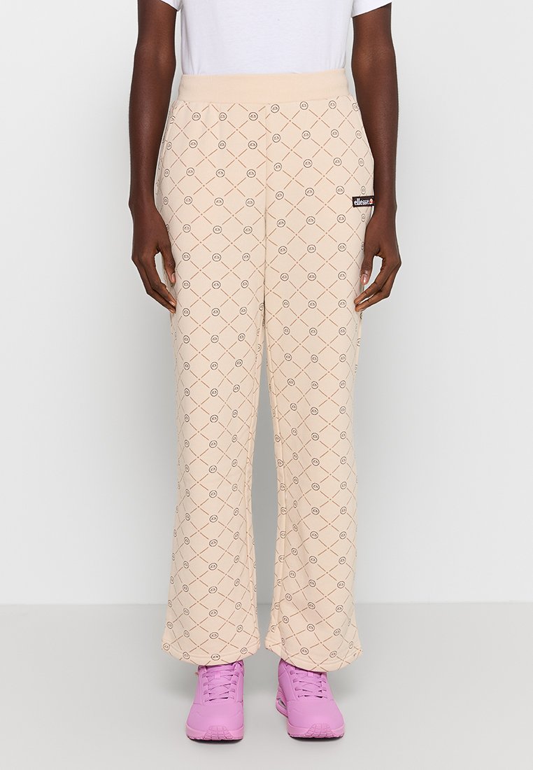 Pantalons larges de couleur crème avec un motif en losanges et un patch logo. Dotés d'une taille douce, fabriqués en tissu tissé. Accentué par des chaussures roses.