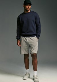 Marinblå sweatshirt med ribbade muddarna, kombinerad med ljusgrå shorts. Vita sneakers och en svart keps fulländar den avslappnade looken. Slät tygkvalitet.