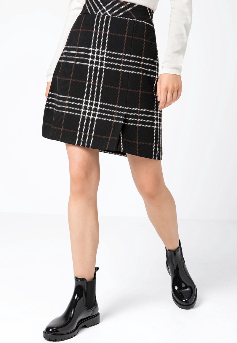 Mustapilkullinen hame, jossa on edessä halkio, valmistettu tekstuuripinnoitteisesta kankaasta, jossa on valkoisia ja ruskeita viivoja. Yhdistetty kiiltäviin mustiin nilkkasaappaisiin.