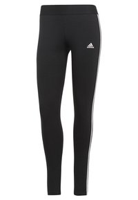 Leggings neri con una superficie liscia, caratterizzati da strisce laterali bianche e una fascia in vita. Un logo Adidas è visibile sulla coscia sinistra.