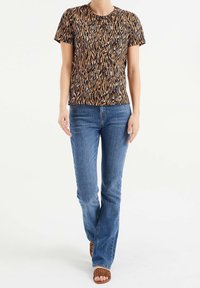 Kortärmad topp i brun och svart djurmönster, kombinerad med ljusblå flarejeans och bruna flätade sandaler. Enkel rund nacke och avslappnad passform.