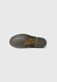 Semelle d'une chaussure noire avec une semelle translucide présentant un motif en grille et un tread texturé pour une adhérence sur un fond uni.