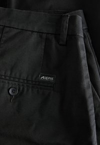Schwarze Hosen aus glattem Stoff verfügen über einen Knopfverschluss, seitliche Taschen und ein Etikett in der Nähe des Bundes mit dem Text "aprel."