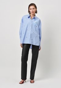 Blue and white striped long-sleeve shirt with decorative metallic accents, paired with black trousers and burgundy heeled sandals.