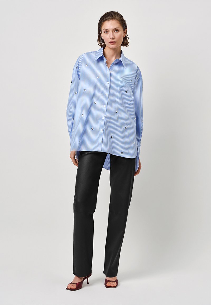 Blue and white striped long-sleeve shirt with decorative metallic accents, paired with black trousers and burgundy heeled sandals.