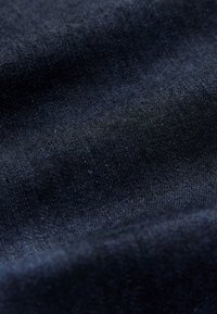 Close-up van donkerblauwe denimstof met subtiele plooien en zichtbaar weefpatroon.