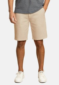 Bermudas color caqui hechas de una mezcla de algodón suave, que presentan un corte holgado, una parte frontal plana y bolsillos laterales, combinadas con zapatillas blancas de cordones.