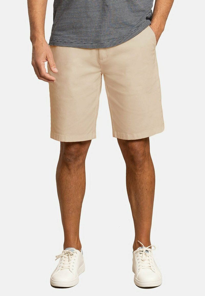 Bermudas color caqui hechas de una mezcla de algodón suave, que presentan un corte holgado, una parte frontal plana y bolsillos laterales, combinadas con zapatillas blancas de cordones.