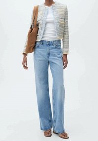 Jean large bleu clair associé à un blazer texturé crème et pastel, superposé à un t-shirt blanc, avec un sac cabas marron.