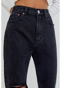 High-waisted black denim jeans with distressed hem. Features five pockets and copper-tone hardware. Textured fabric with a classic fit.